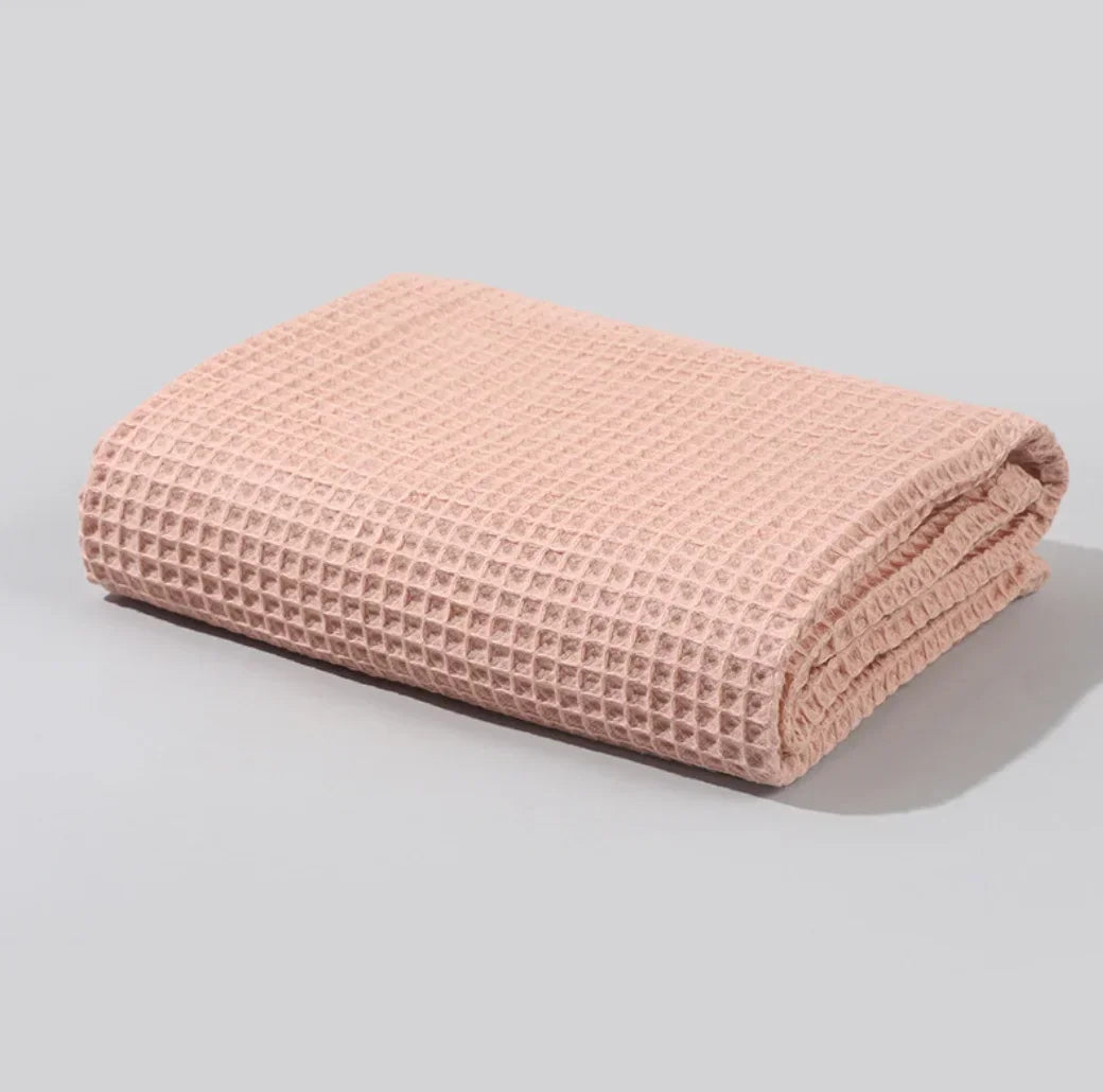Folded pastel pink waffle weave textured towel on a light gray surface